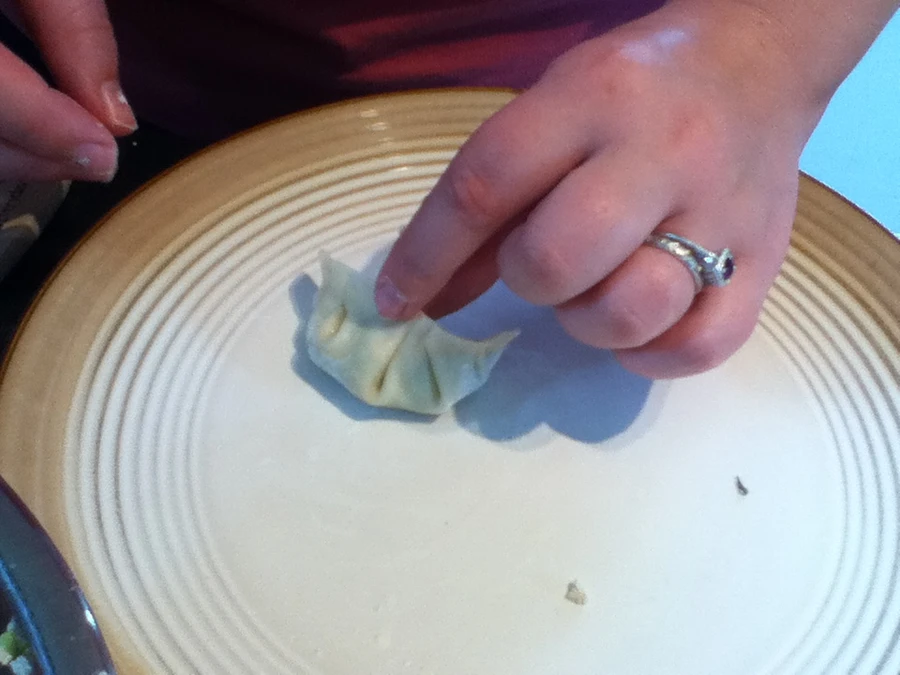 Illustrative scene of hands shaping a jiaozi dumpling over a plate