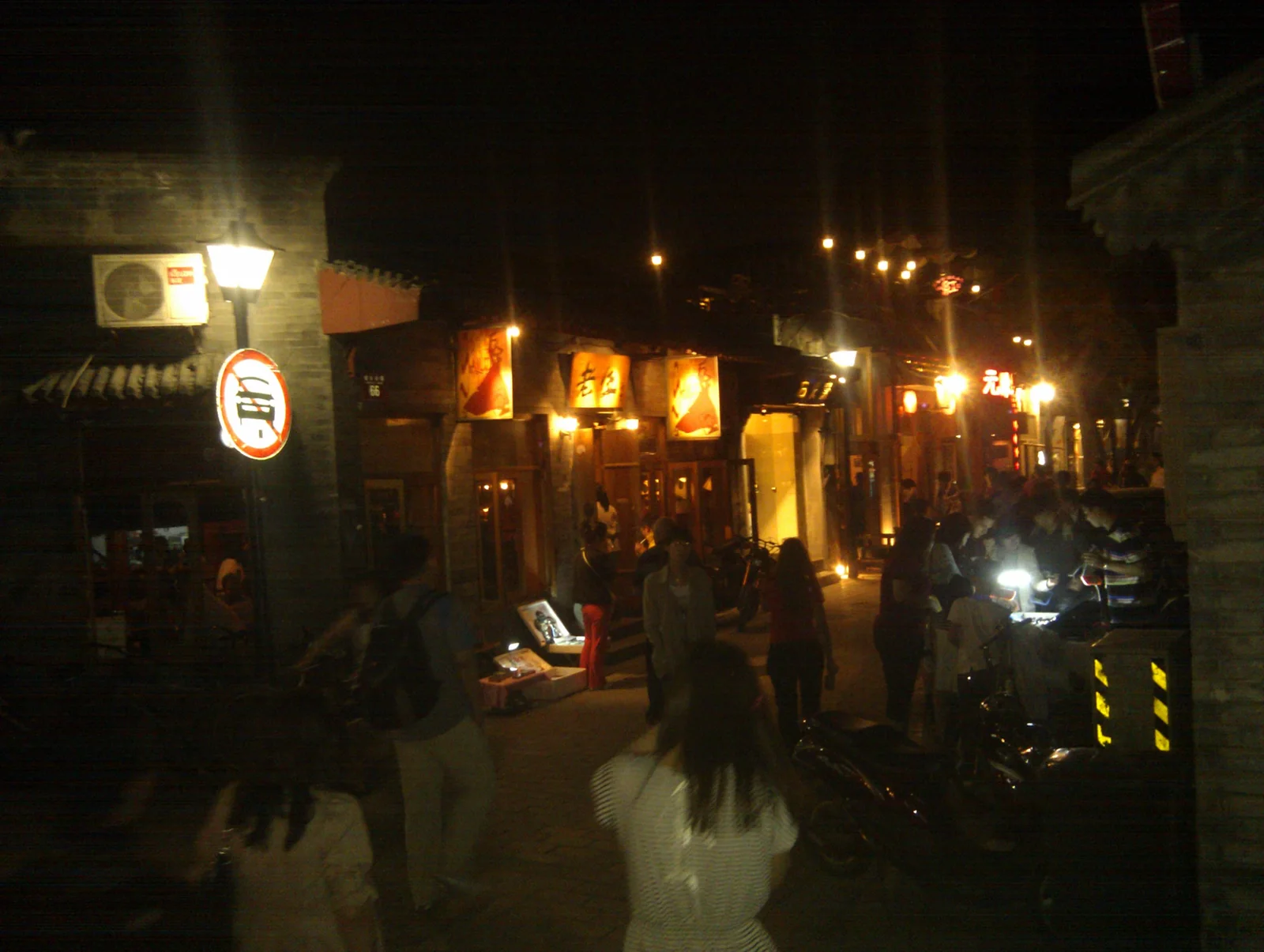 People walking between lit shopfronts on Nanluoguxiang at night in Beijing