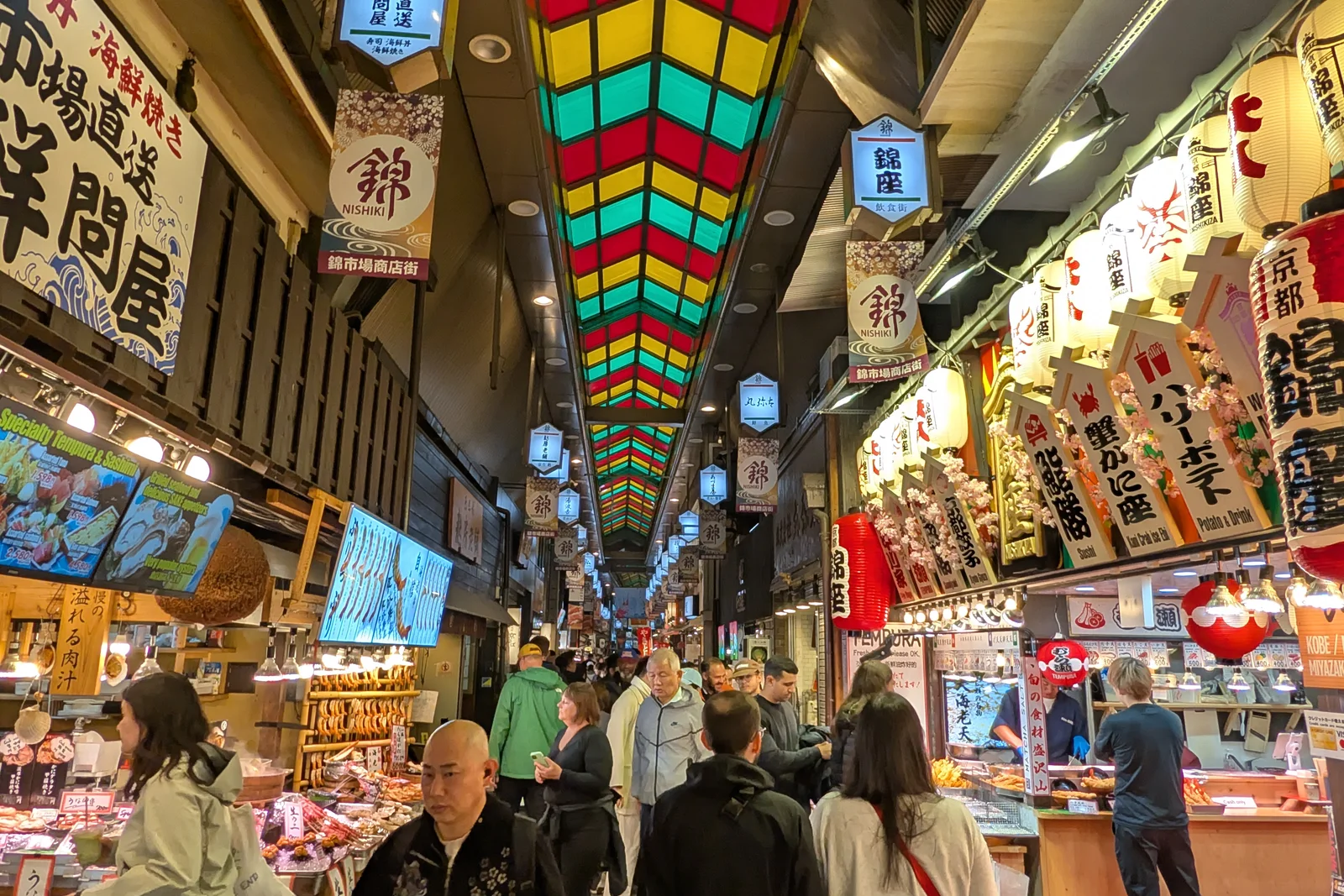 Visitors and food stalls beneath the colourful covered roof of Nishiki Market in Kyoto